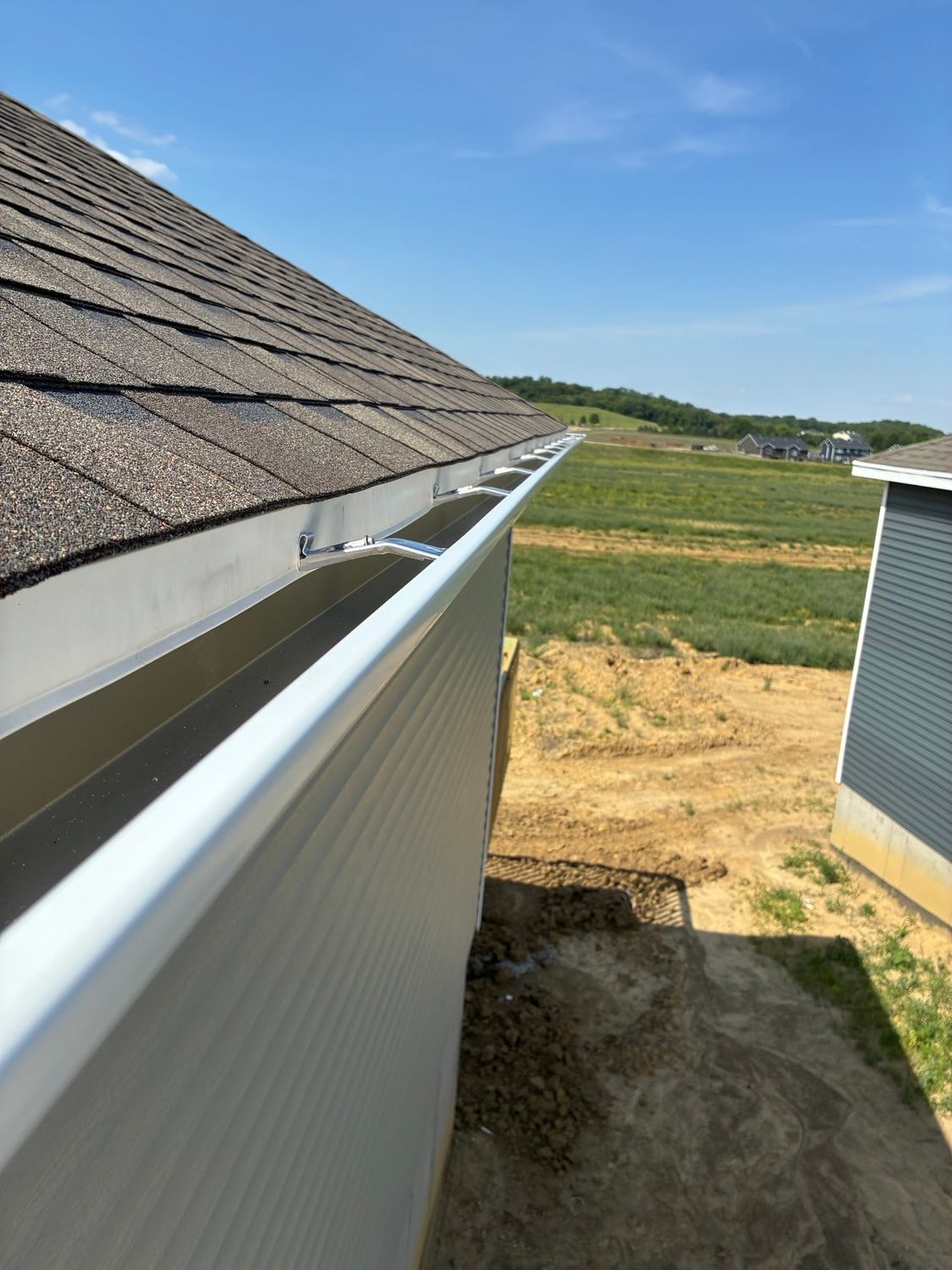 Roof gutter along house roofline beside a dirt yard under a clear blue sky