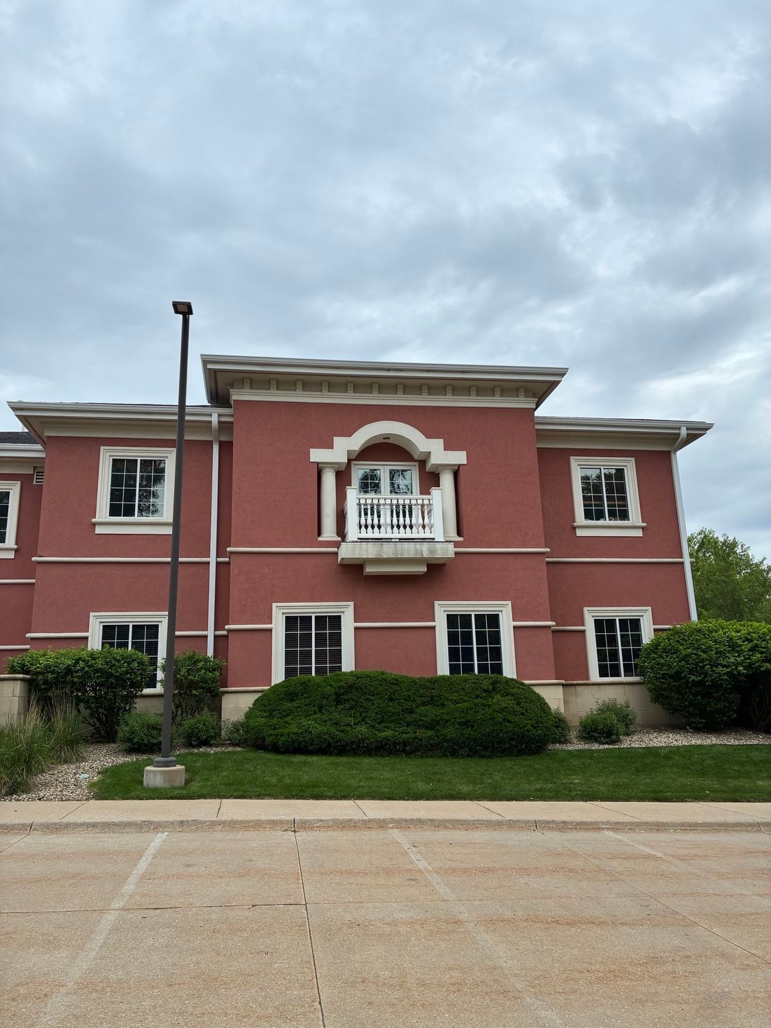 Pink two-story building with white trim and central balcony under a cloudy sky