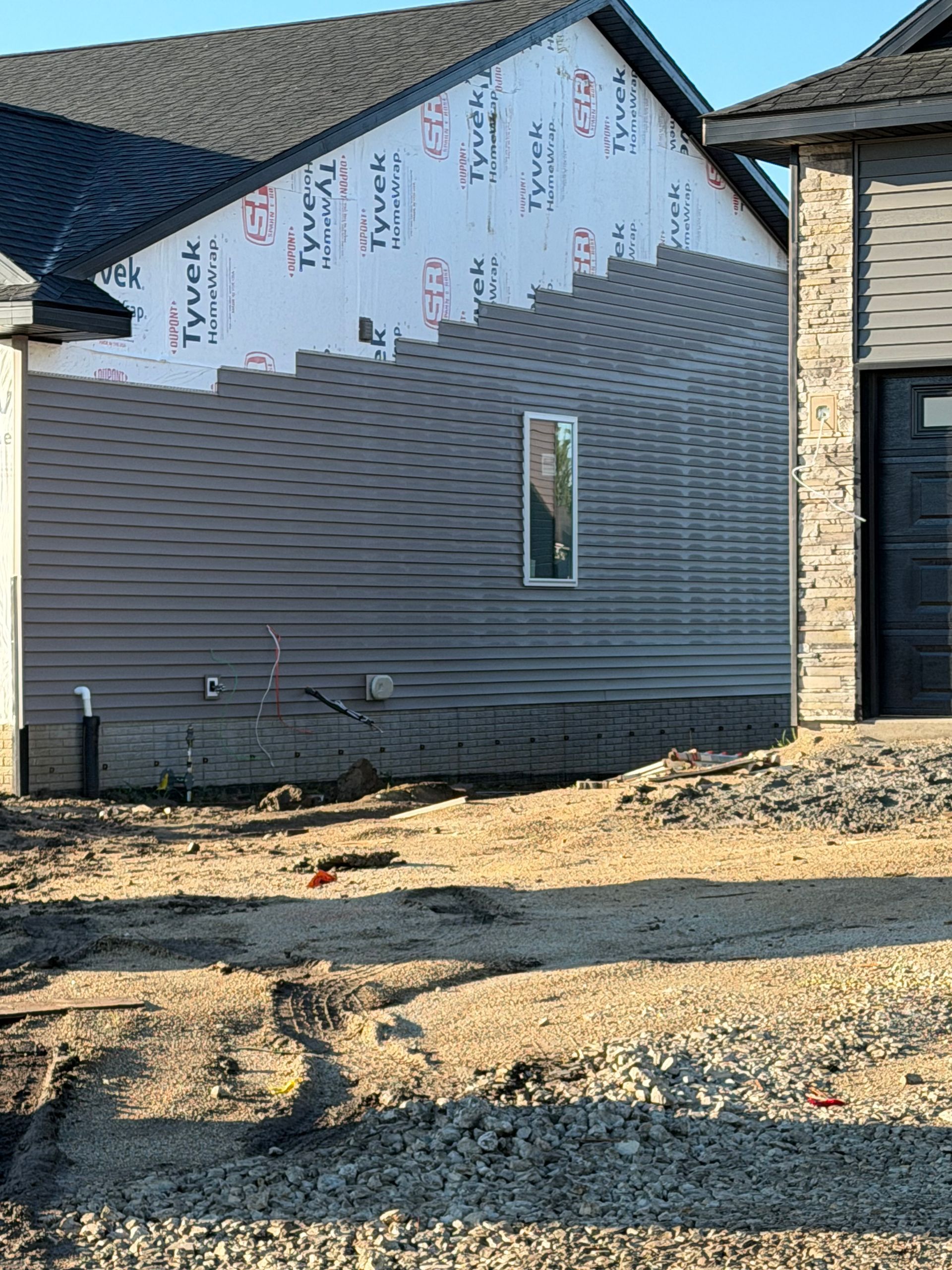 Partially constructed house with gray siding, exposed sheathing, and gravel in front