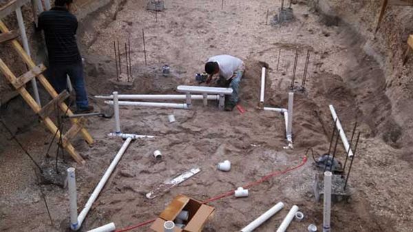 Two men are working on a swimming pool in the dirt.