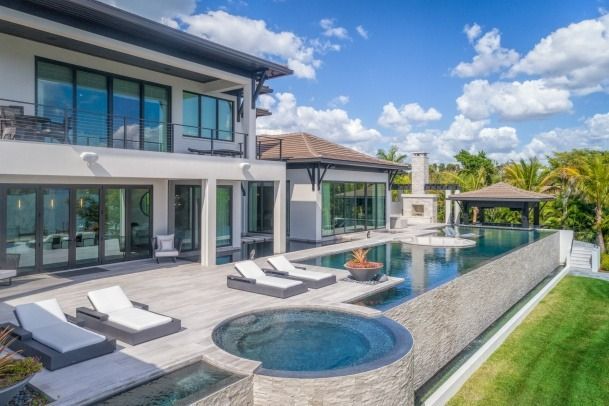 A large house with a swimming pool and lounge chairs in front of it.