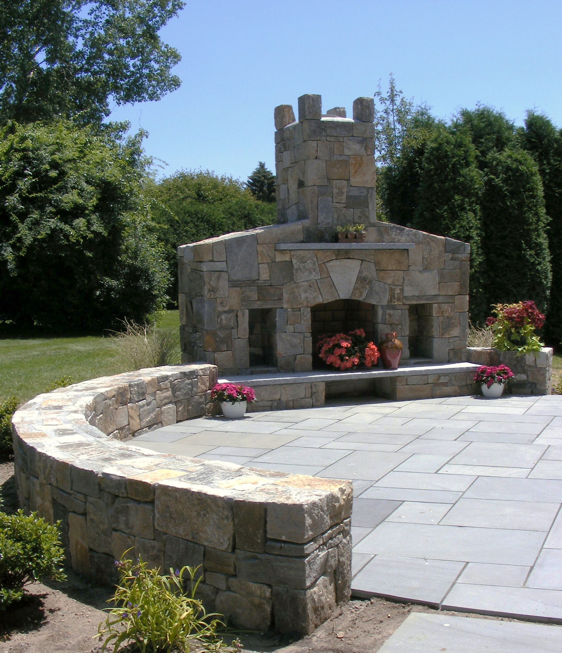 A stone fireplace is surrounded by flowers on a patio