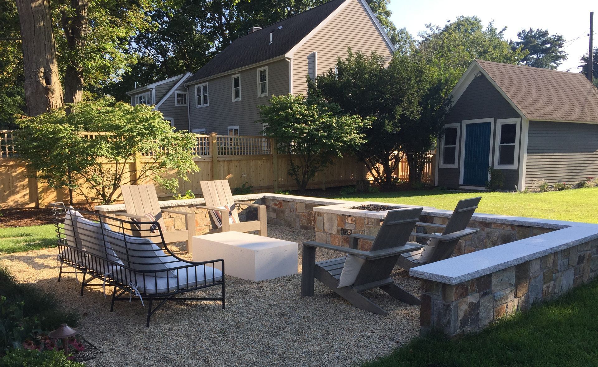 A backyard with a fire pit and chairs in front of a house.