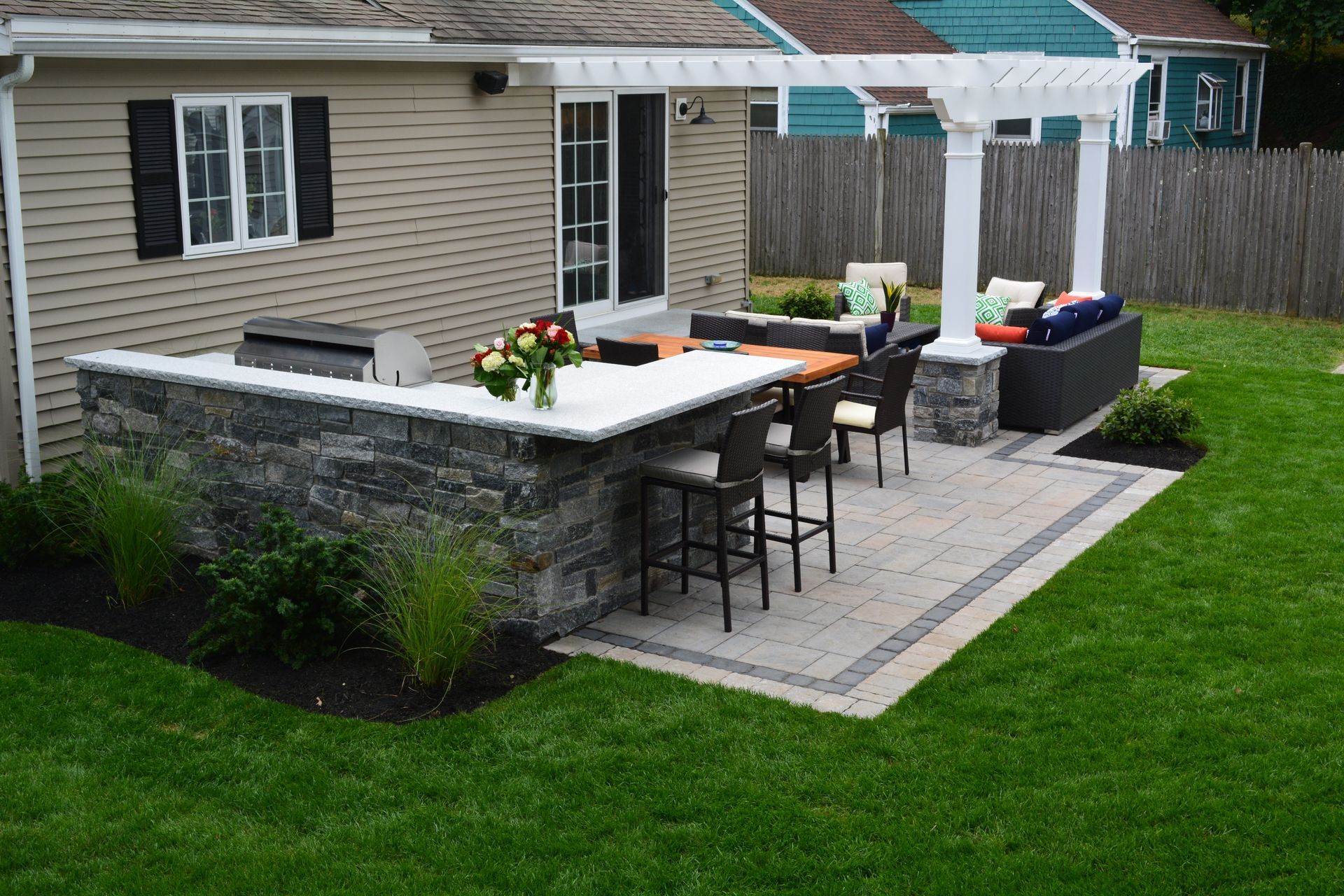 A patio with a grill and a pergola in the backyard of a house.