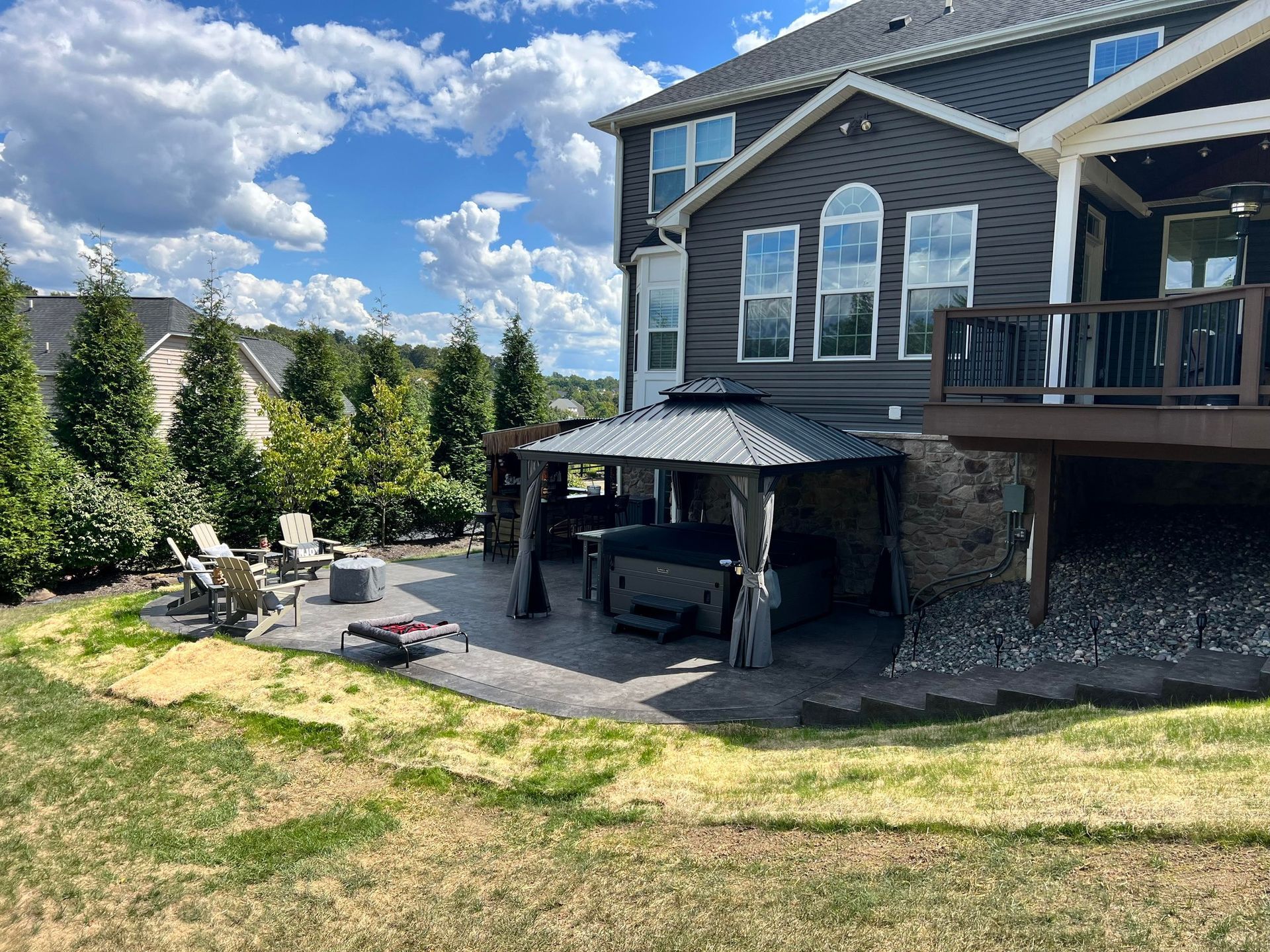 Backyard with patio, hot tub under gazebo, and deck extending from a two-story house.
