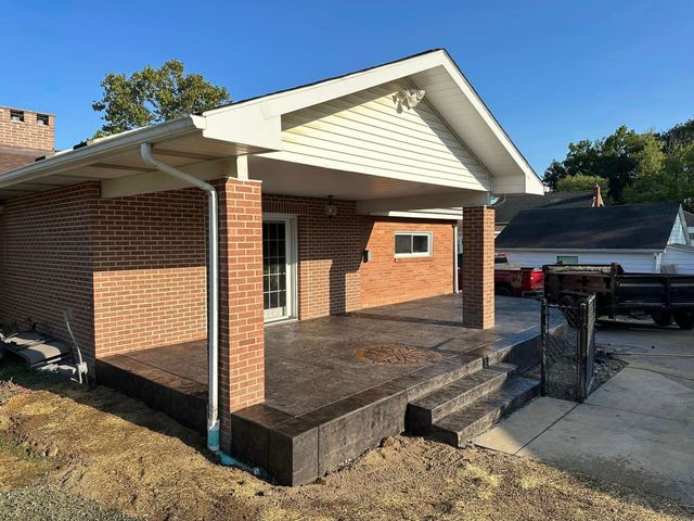 Brick building with covered porch and steps; concrete patio; blue sky.