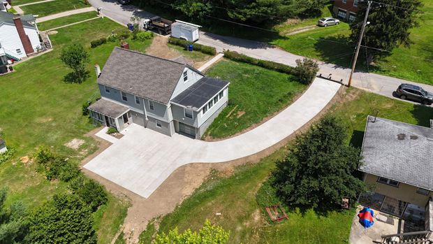 Aerial view of a gray house with a concrete driveway and surrounding green lawn.