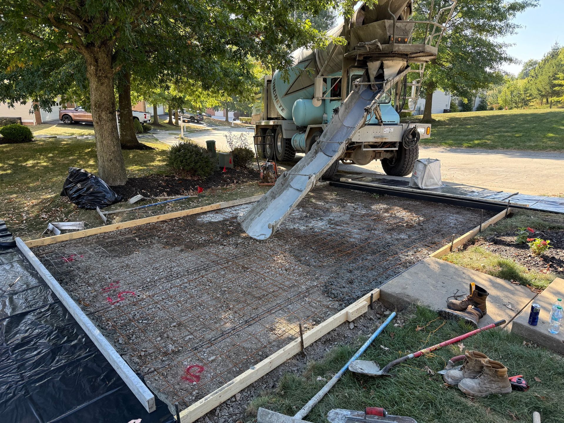 Cement truck pouring concrete into a framed area for a new patio, outdoors on a sunny day.