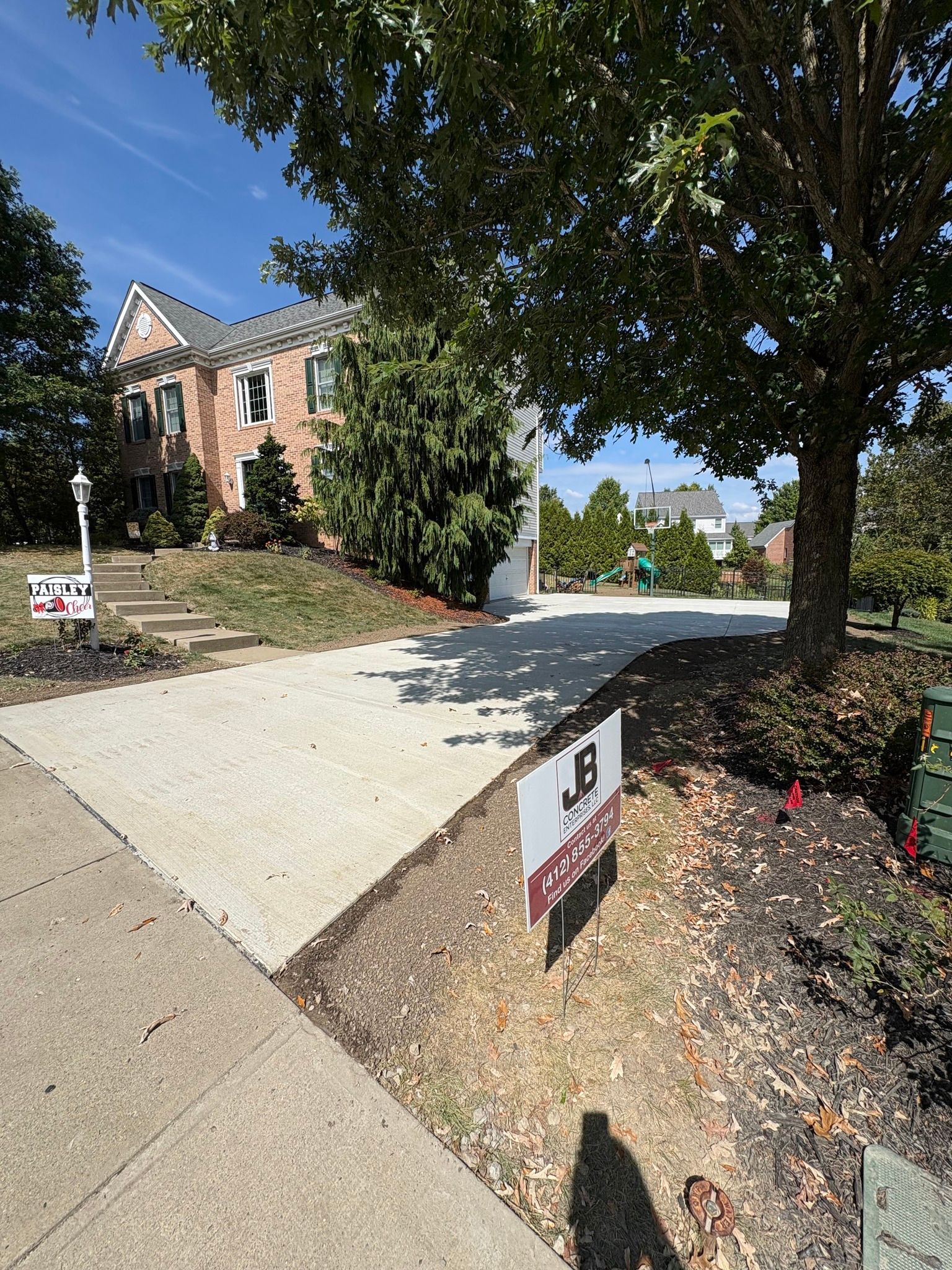 Concrete driveway leading to a brick house with a front yard. A tree casts a shadow on the driveway.