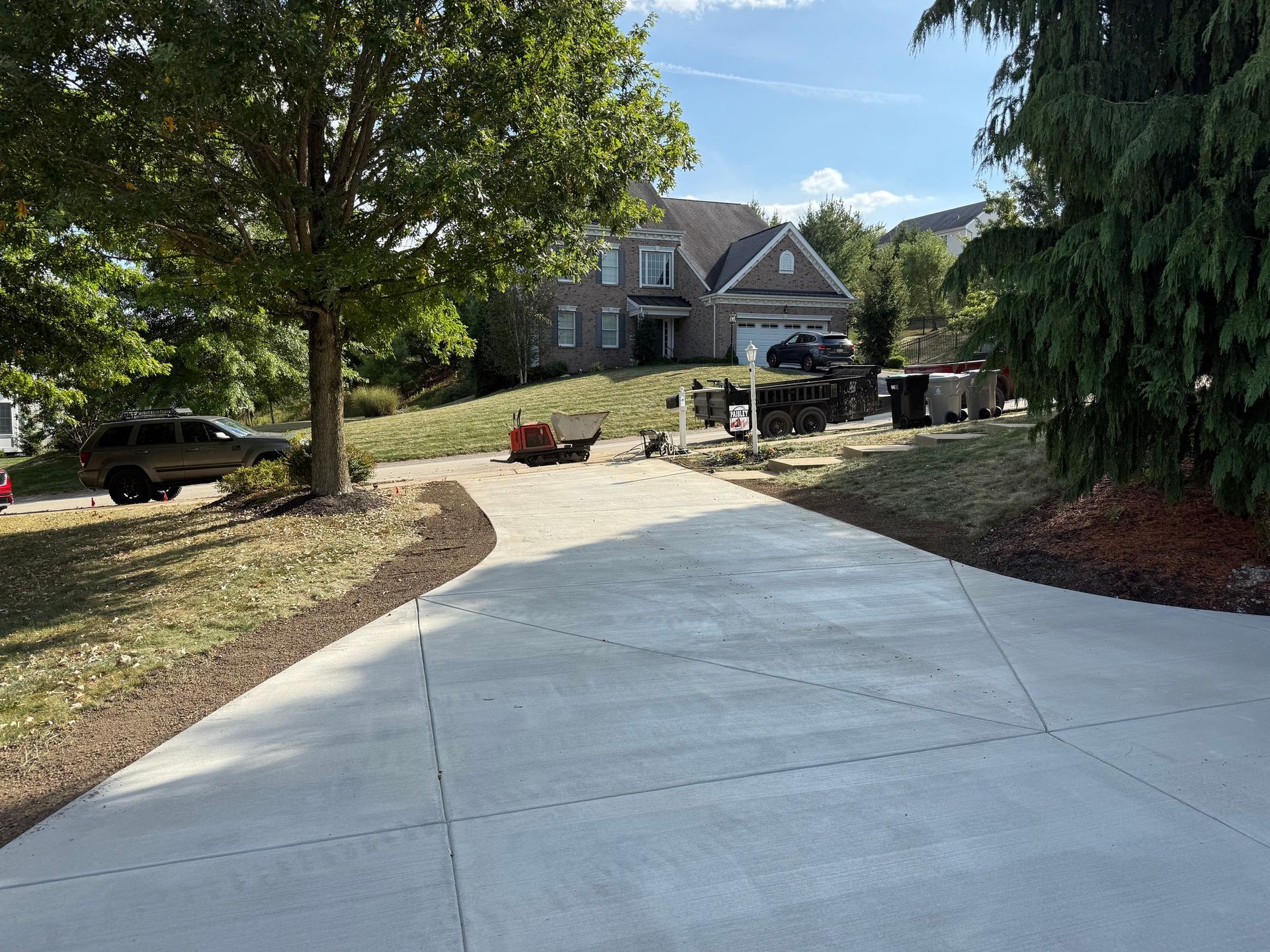 A paved driveway leading to a two-story house with a lawn. A car is parked to the left.
