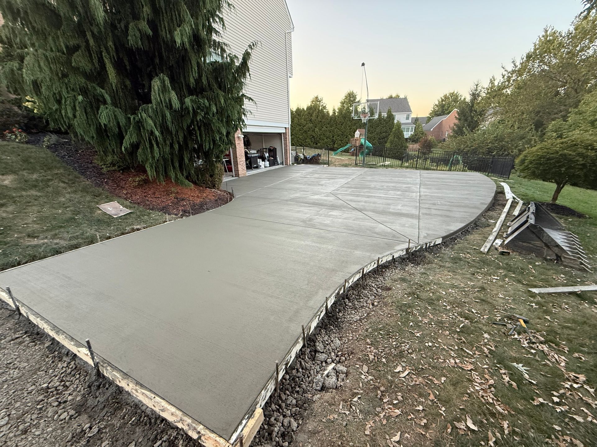 Freshly poured concrete driveway in front of a house, surrounded by lawn and trees.