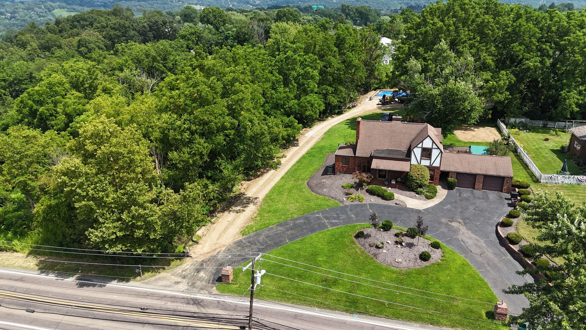 Aerial view of a house with a brown roof and a black driveway surrounded by green trees.