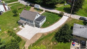 Aerial view of a gray house with a concrete driveway and surrounding green grass and trees.