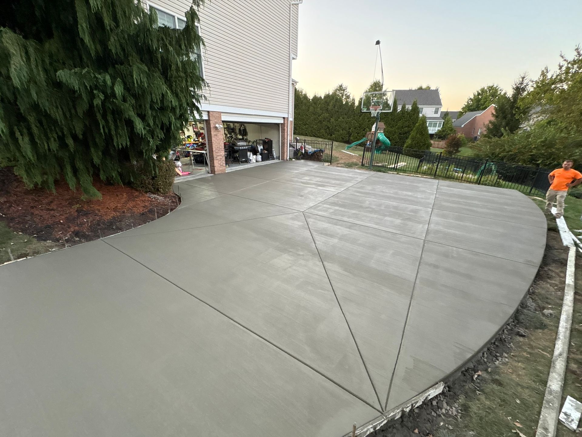 Freshly poured concrete driveway with workers. Gray cement, curved edge, garage in the background.