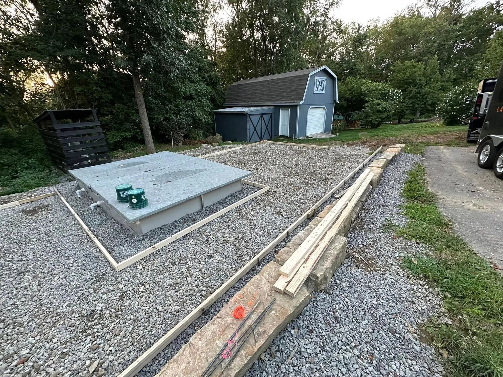 Gravel yard with a gray septic tank, a blue shed, and wooden edging.