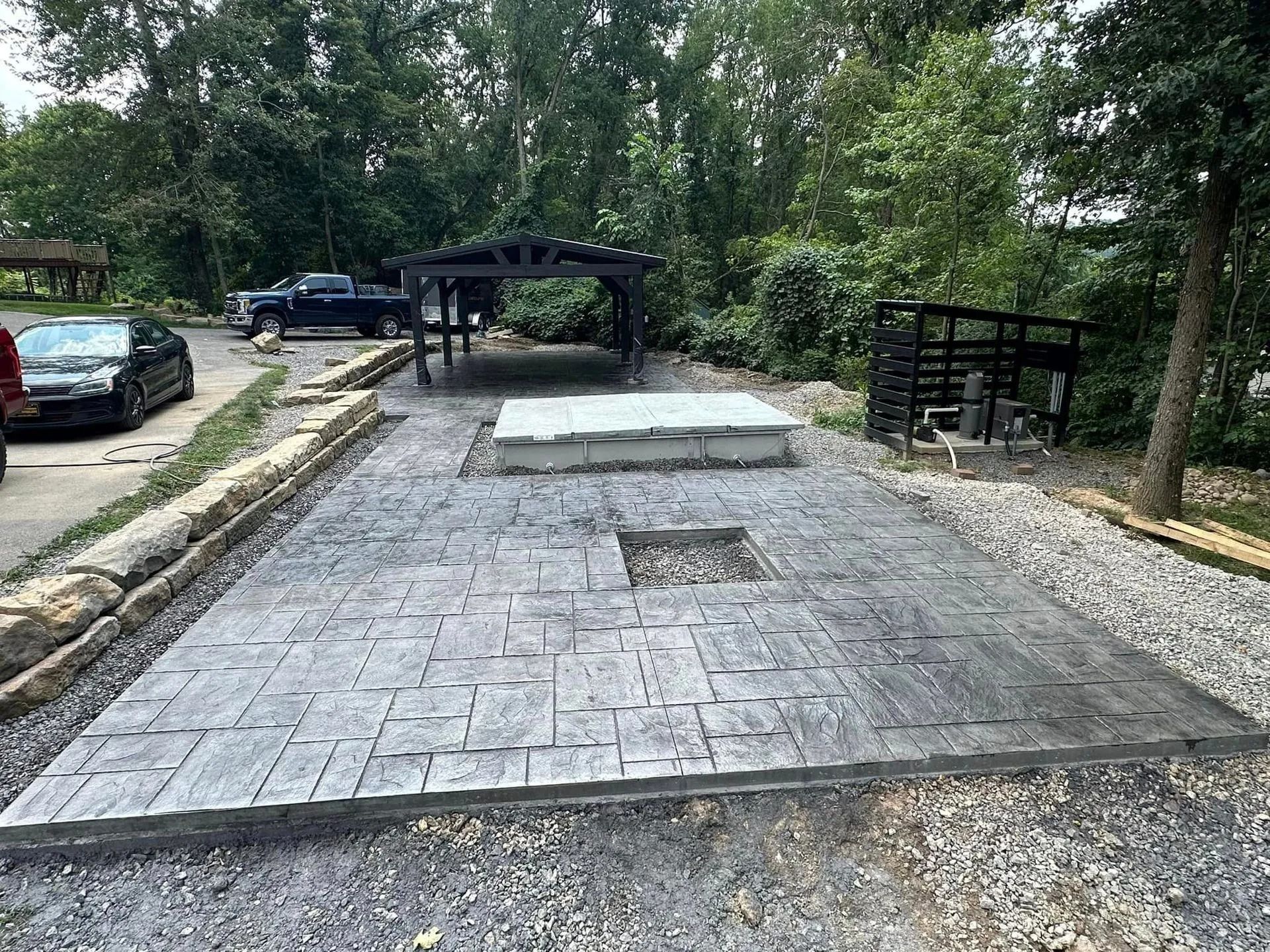 Gray stamped concrete patio with pergola, fire pit opening, and landscaping.