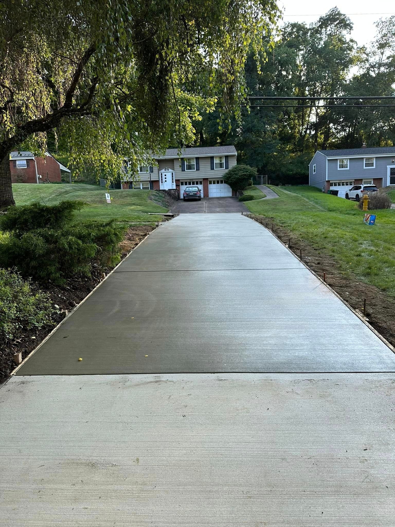 Newly poured concrete driveway leading to a house, flanked by grass and greenery.