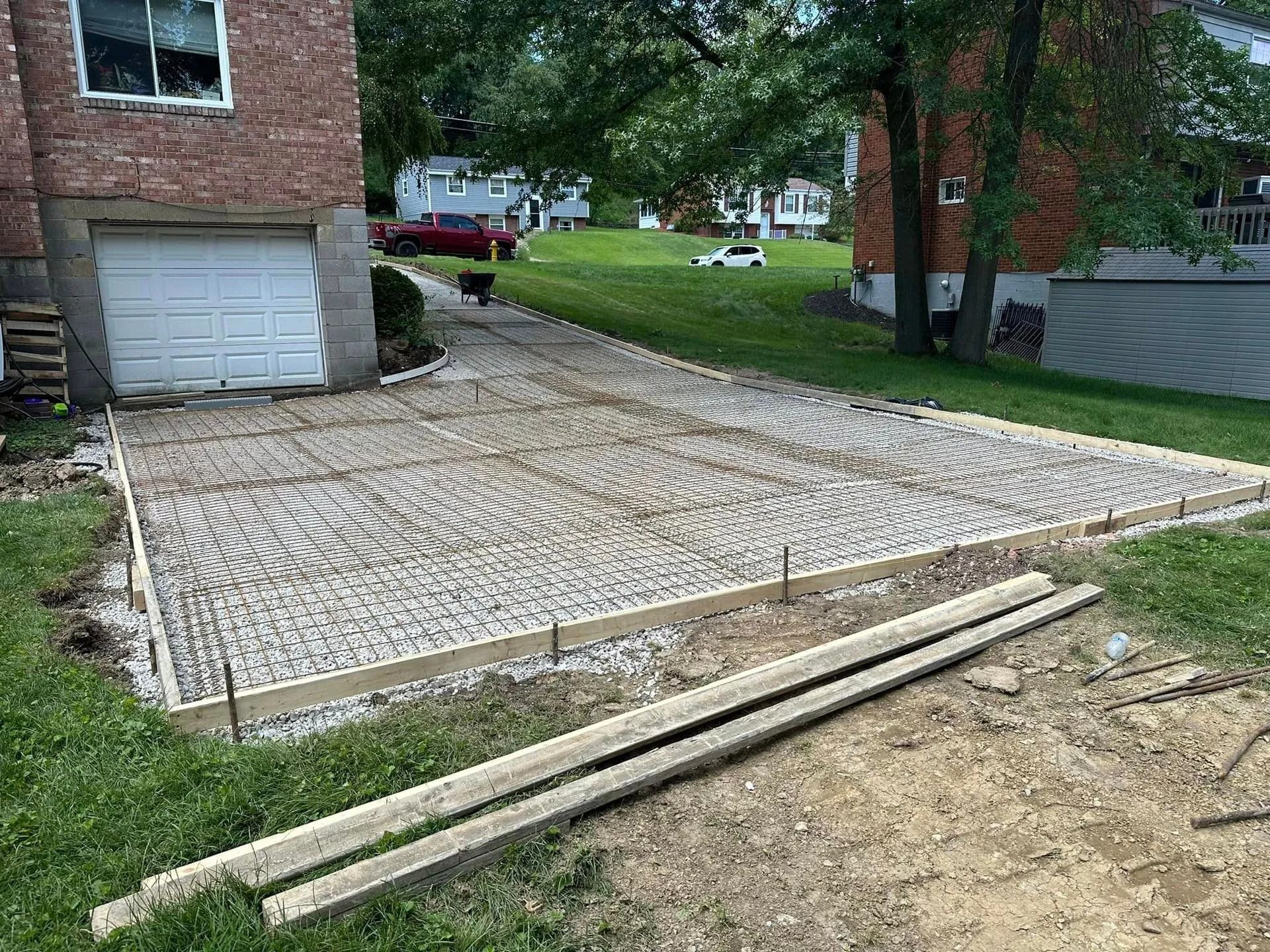 Driveway under construction with wooden forms and exposed gravel base, next to a brick house and grass.