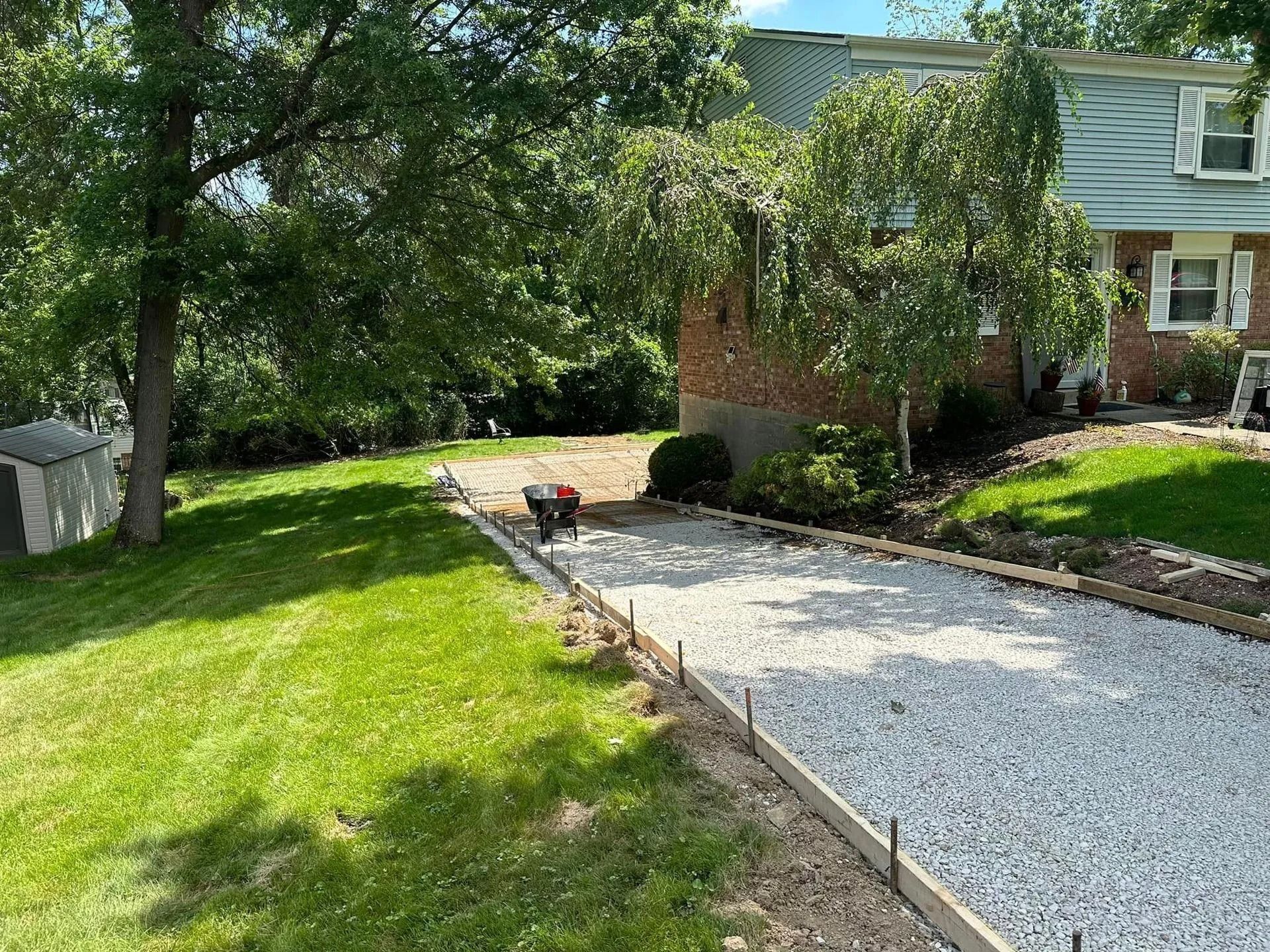 Gravel driveway under construction next to green lawn and a brick and siding house.