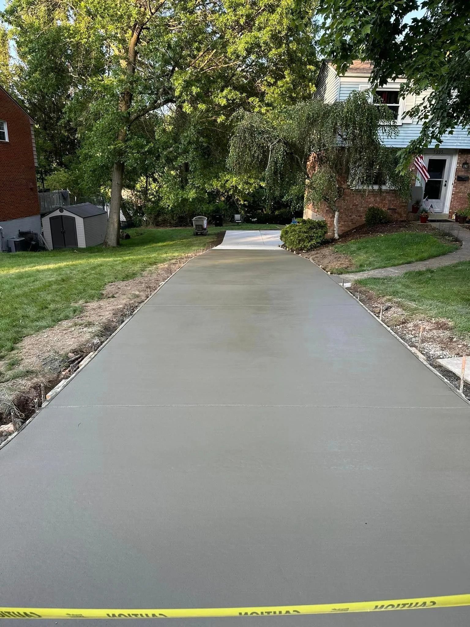 Freshly poured concrete driveway in front of a house. Yellow caution tape is across the bottom.