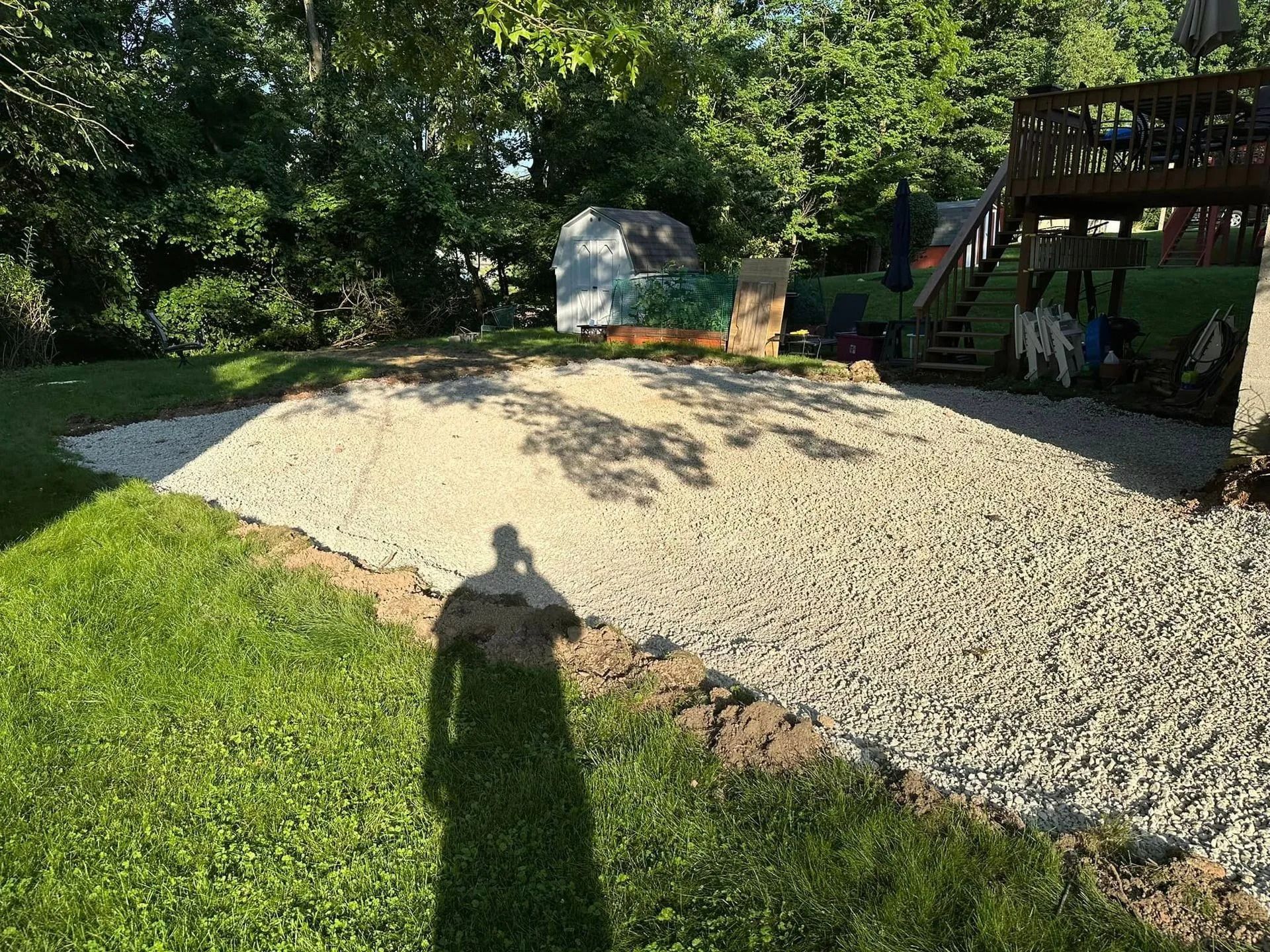 Gravel-covered yard with a playset on the right and a painted shed in the background; sunny day.