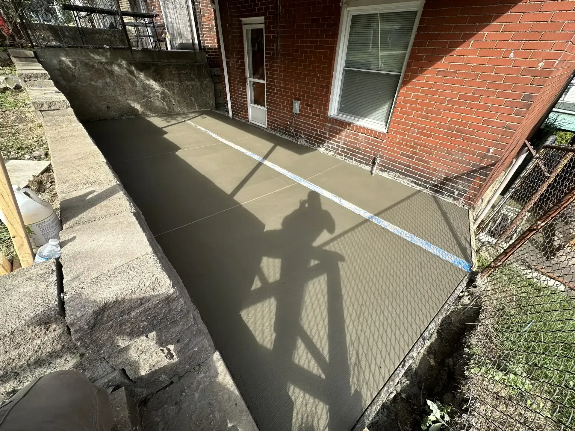 Newly poured concrete patio next to a brick house. A shadow is cast on the surface.
