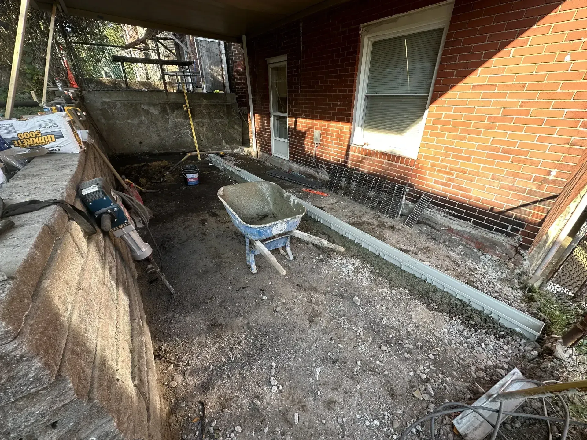 Construction site: dirt, tools, wheelbarrow, brick building. A covered porch is being renovated.