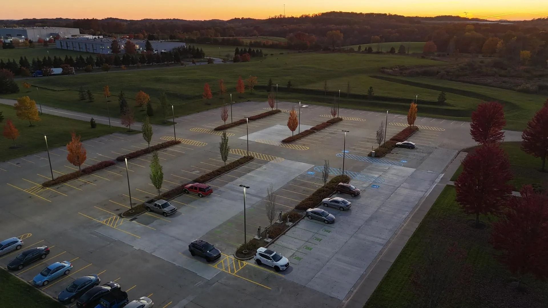 Aerial view of an empty parking lot with cars parked. Trees with autumn leaves are spaced throughout.