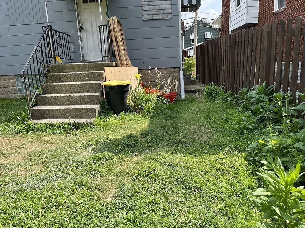 Backyard with concrete stairs, overgrown grass, wooden fence, and a gray house.