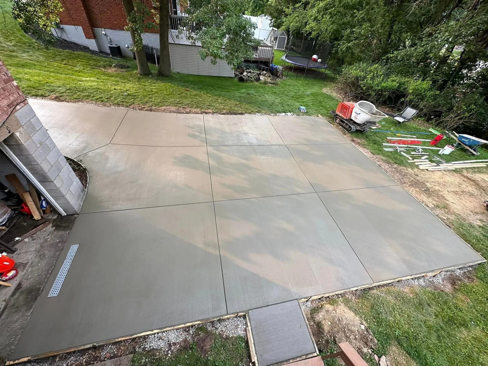 Newly poured concrete patio, divided into sections, in a backyard setting.