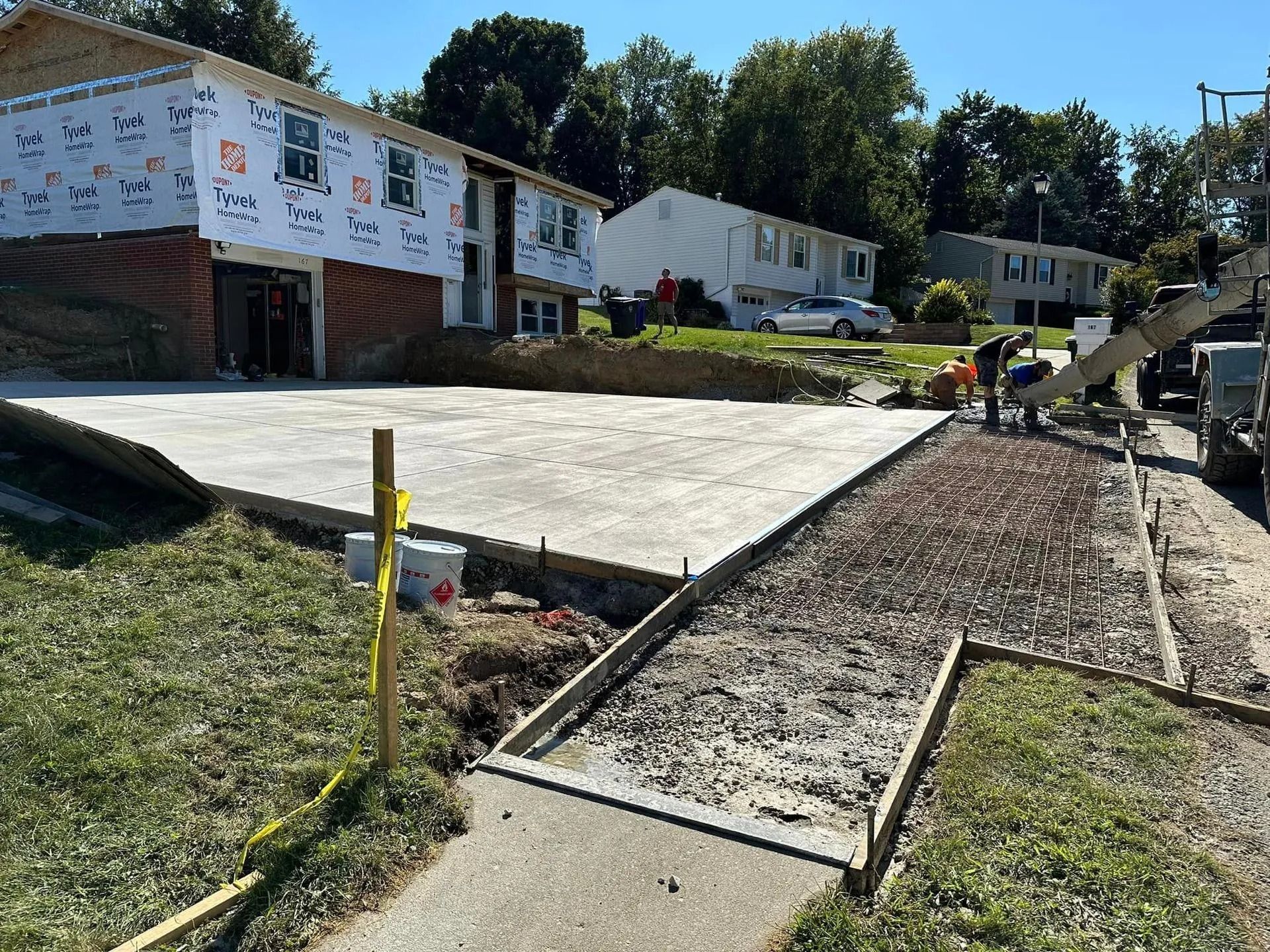 Construction site: concrete pouring for driveway and sidewalk next to a two-story house.