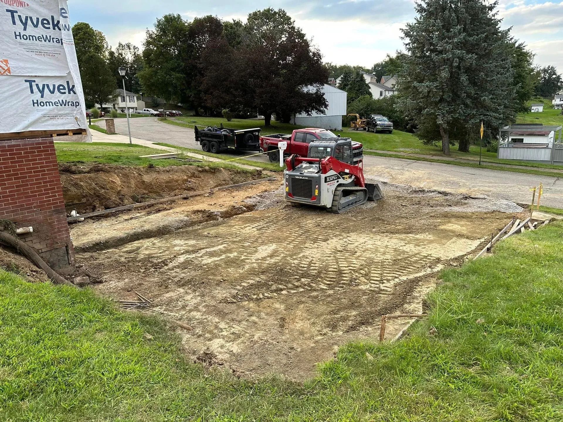 Mini excavator grading a construction site for a foundation, with gravel and a partially built structure nearby.