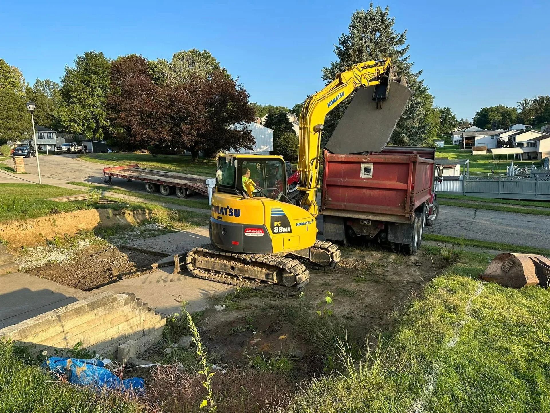 Yellow excavator loading debris into a red dump truck on a construction site.