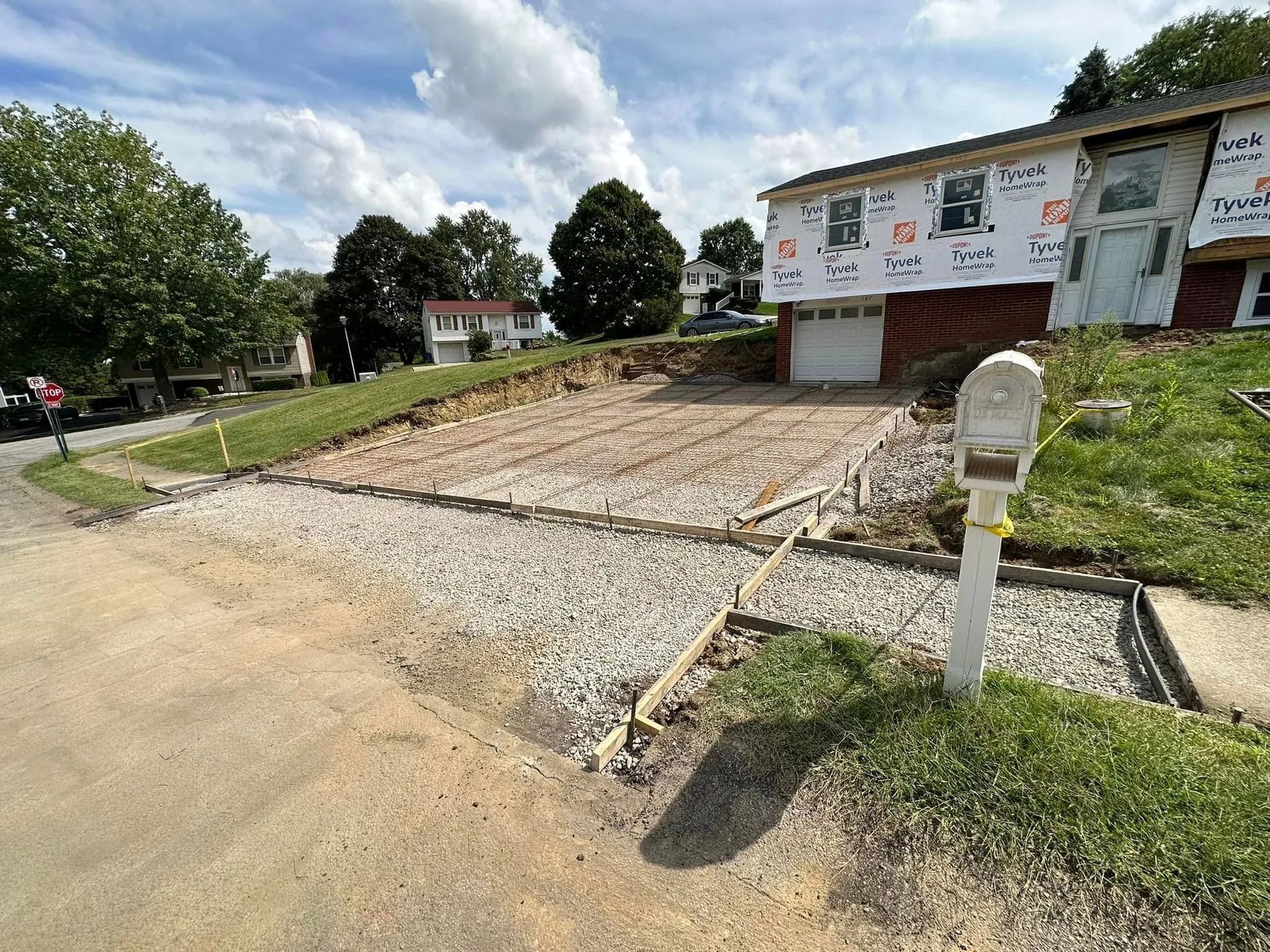 Driveway construction at a two-story house. Gravel base prepared for concrete. Mailbox on the right.