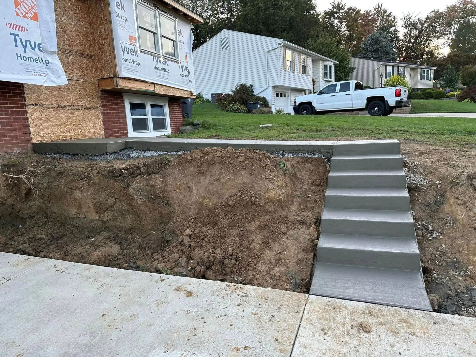 Concrete steps and walkway leading to a house under construction. Dirt and a white pickup truck are visible.