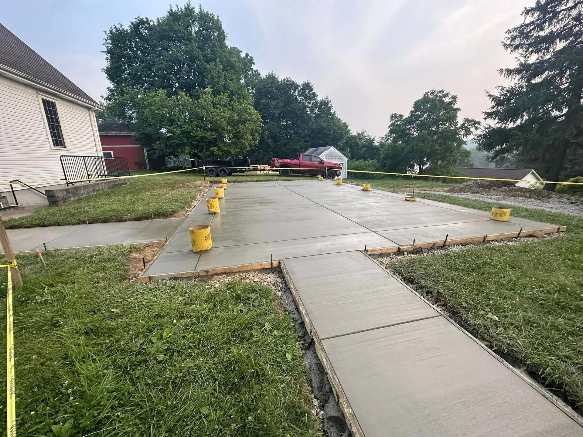 Newly poured concrete driveway and sidewalk with yellow supports. Green grass surrounds it.