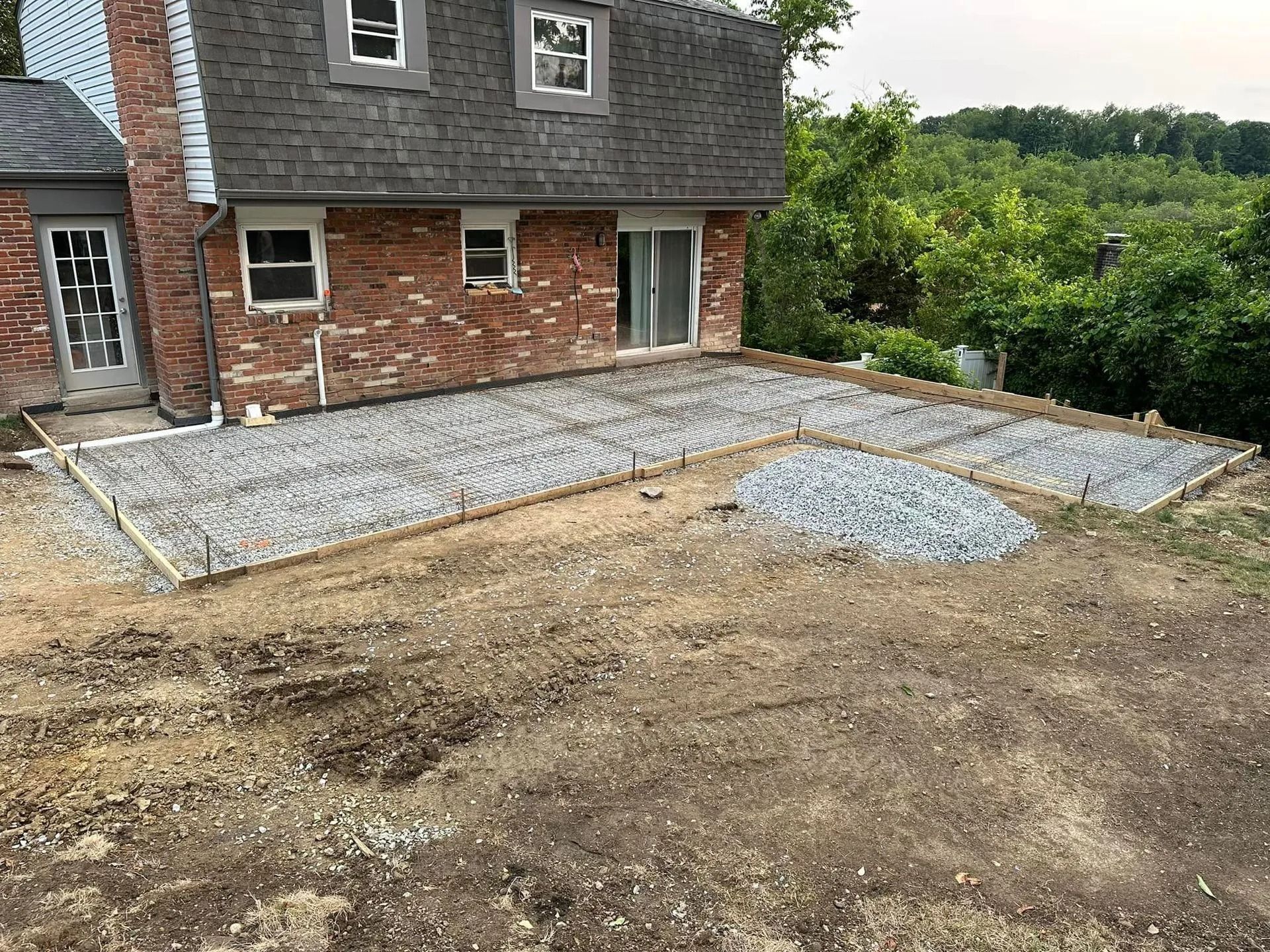 Preparation for a concrete patio; gravel base and wood forms in place next to a brick house.