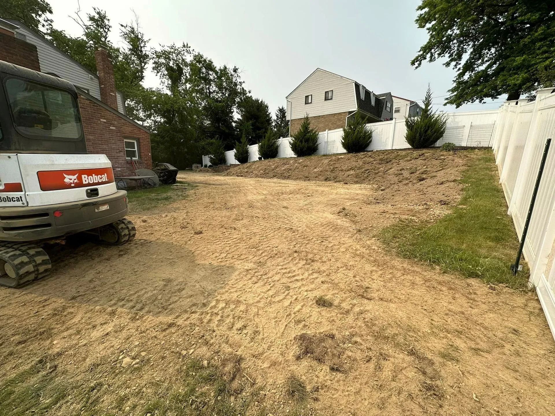 A construction site with a Bobcat excavator, dirt, and a white fence.