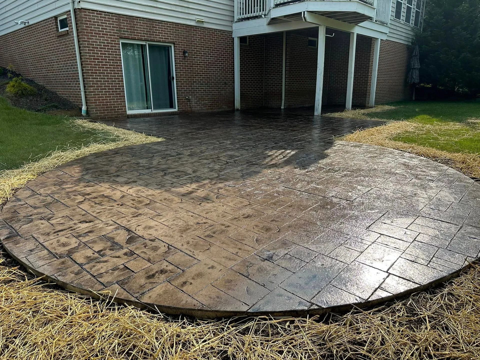 Circular stamped concrete patio outside a brick home; grass surrounds it.