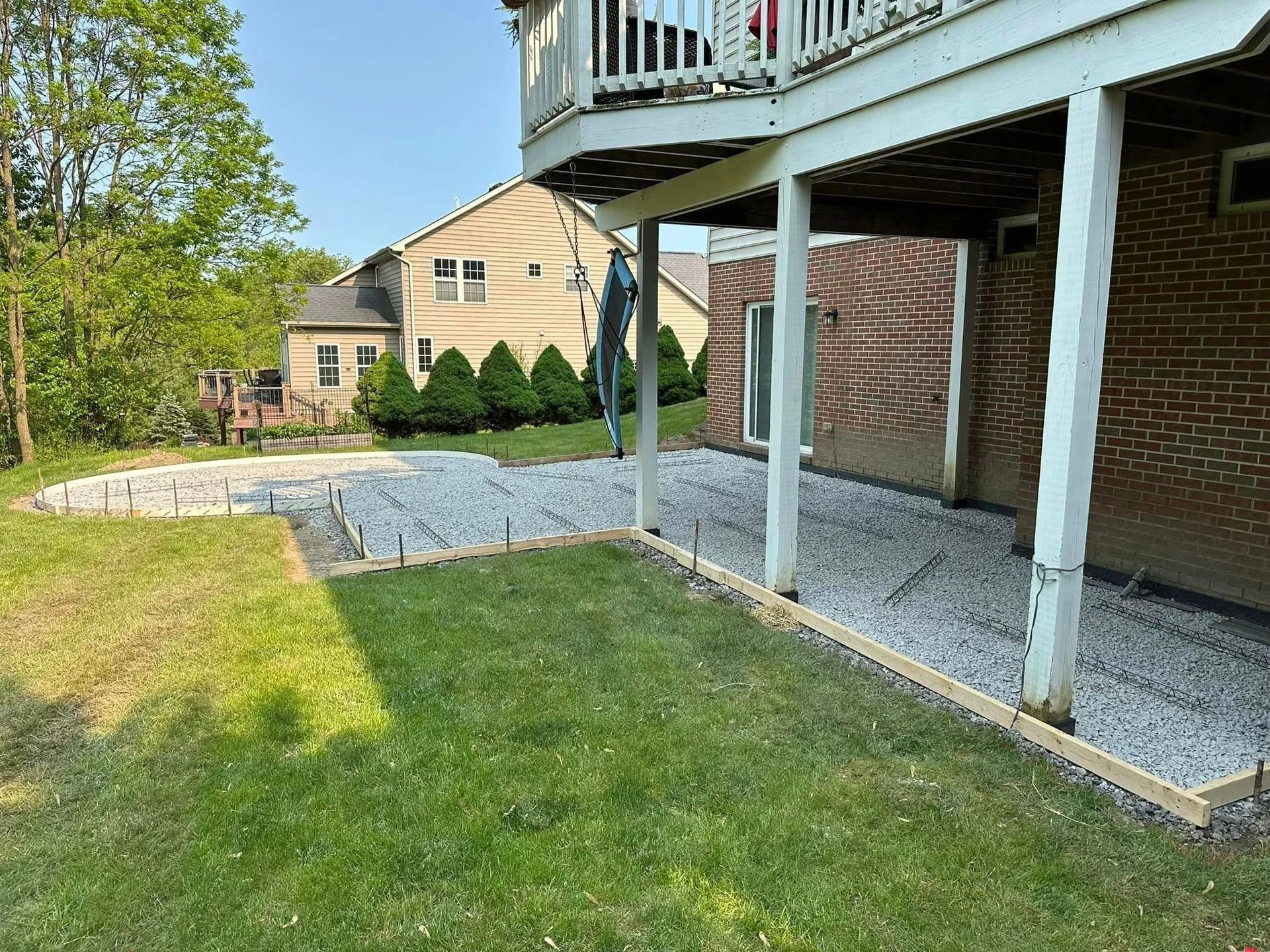 Gravel base with wooden borders under a deck. Part of a building with brick and grass in a yard.