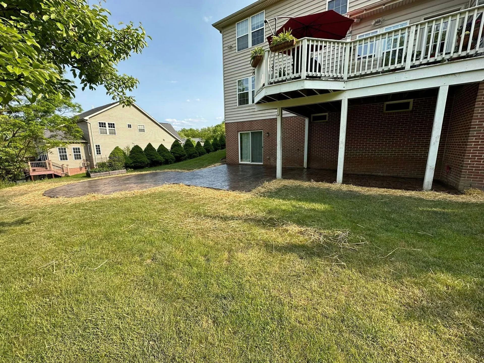 Backyard view of a house with a deck, patio, and green grass on a sunny day.
