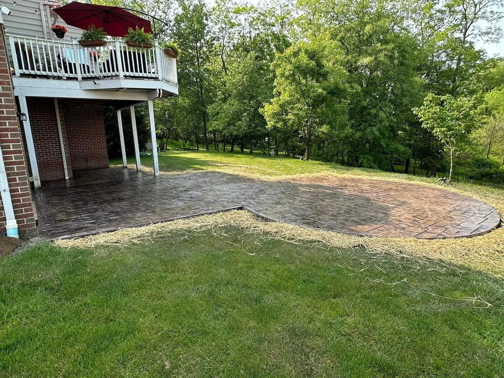 Backyard patio beneath a deck, surrounded by grass and trees.