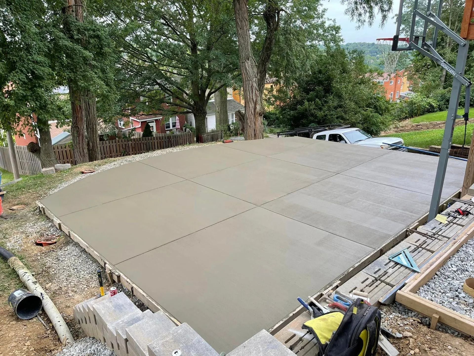 Newly poured concrete slab for a basketball court, surrounded by a wooden frame and landscaping.