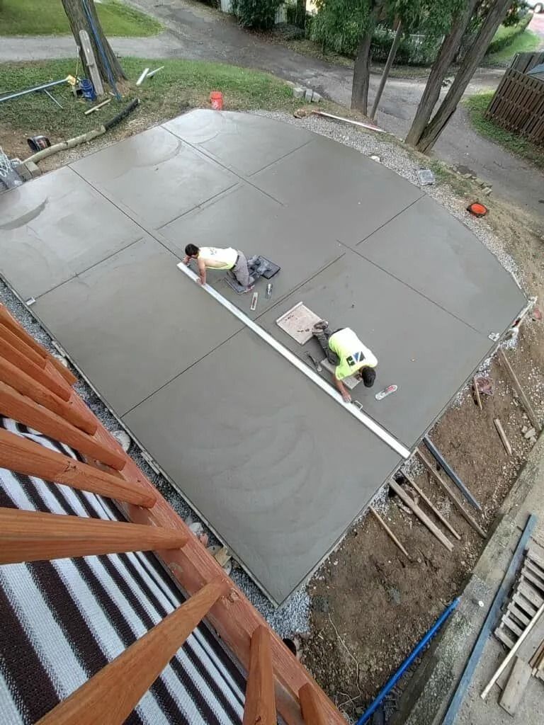 Two workers smoothing wet concrete on a large, square outdoor patio, seen from above.