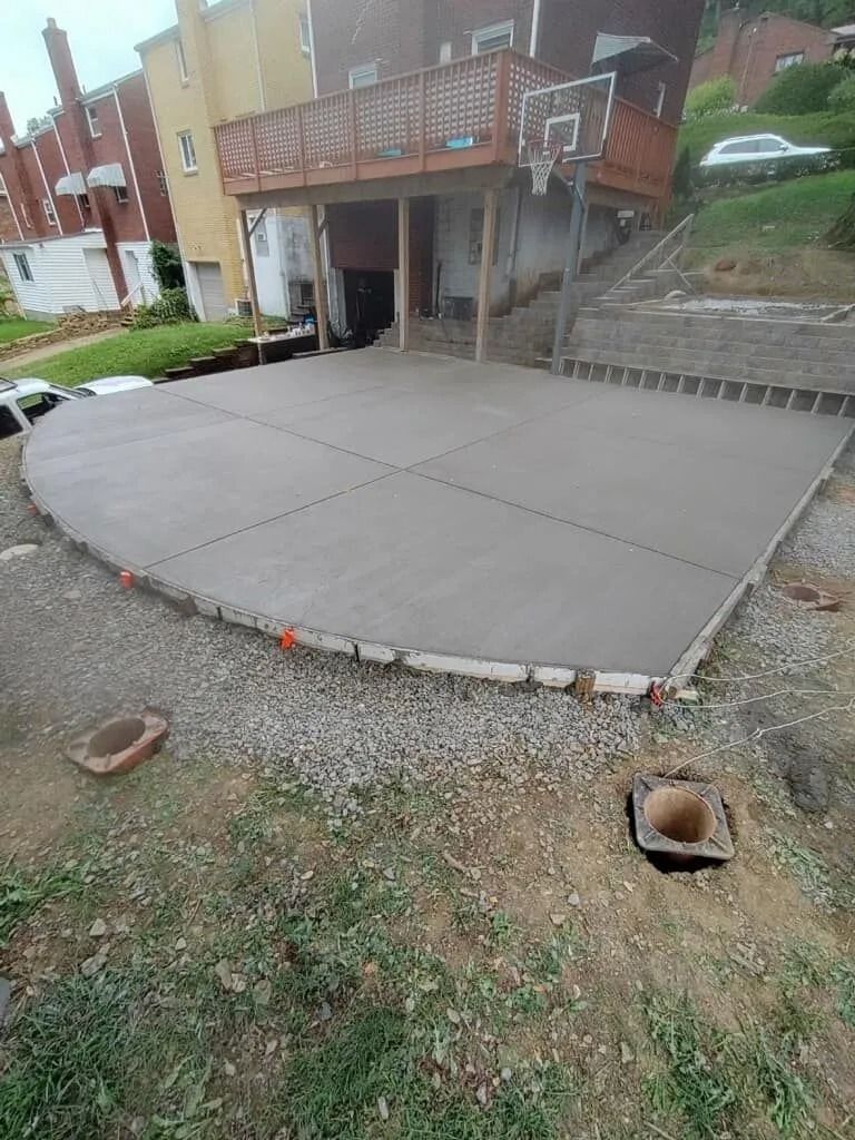 Newly poured concrete patio, bordered by brick and gravel, beneath a wooden deck and house.
