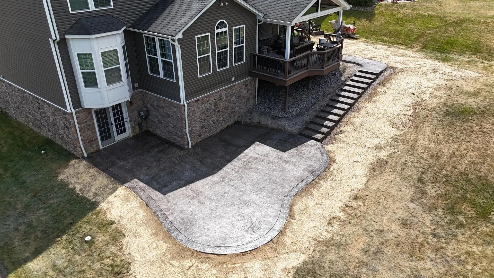 A two-story house with a brick facade and a patio. A retaining wall and stairs lead to a deck.