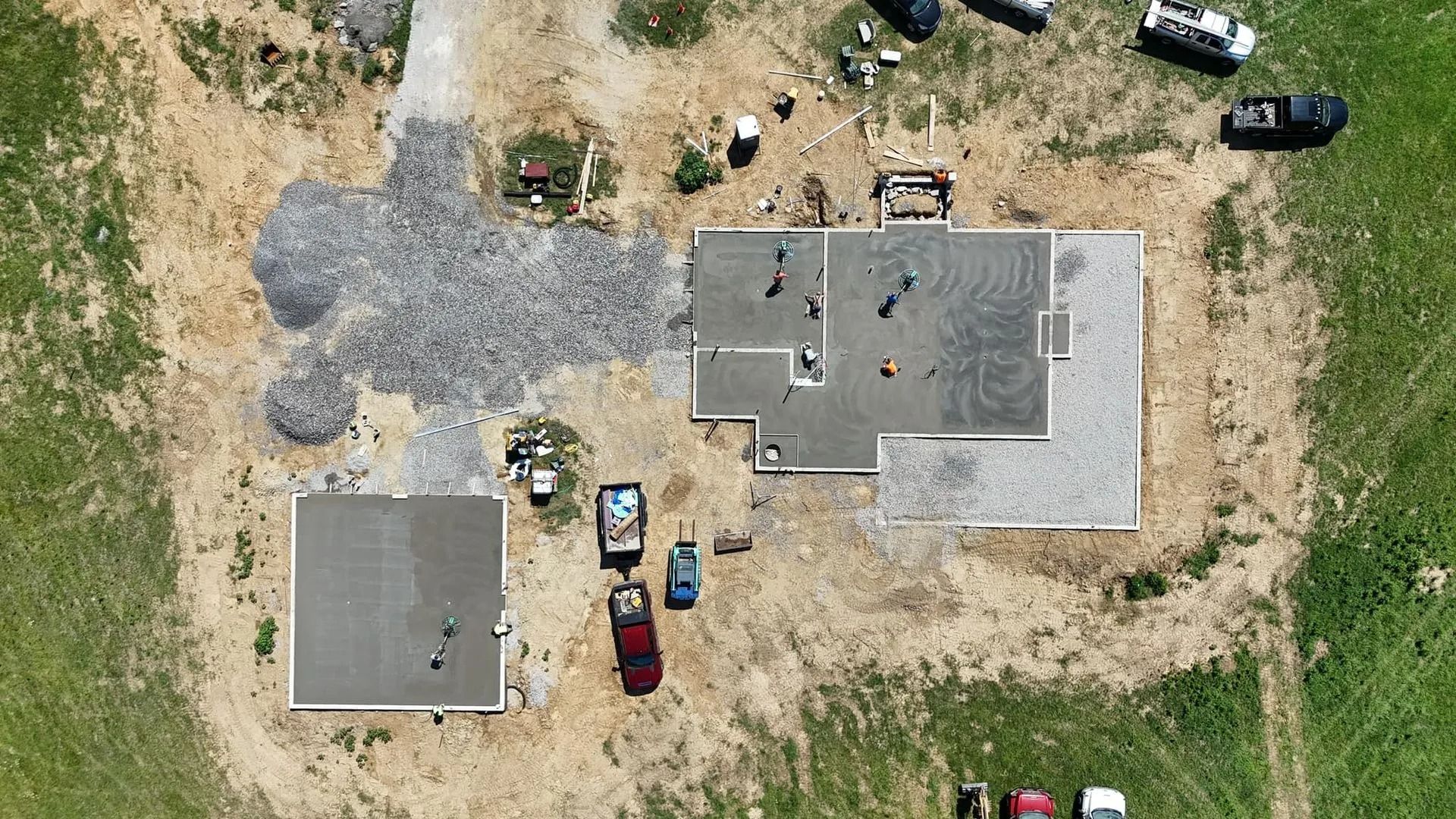 Aerial view of a building under construction, showing concrete foundations and construction equipment on a grassy lot.