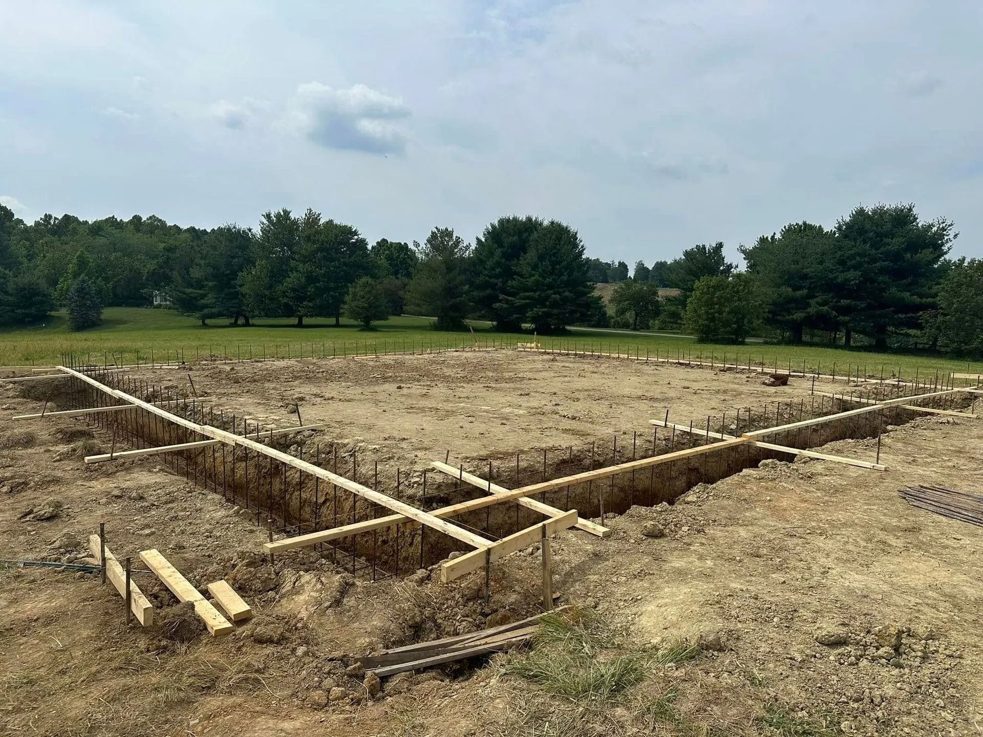 Foundation for a building, with wooden forms in a dug-out area, set in a field.