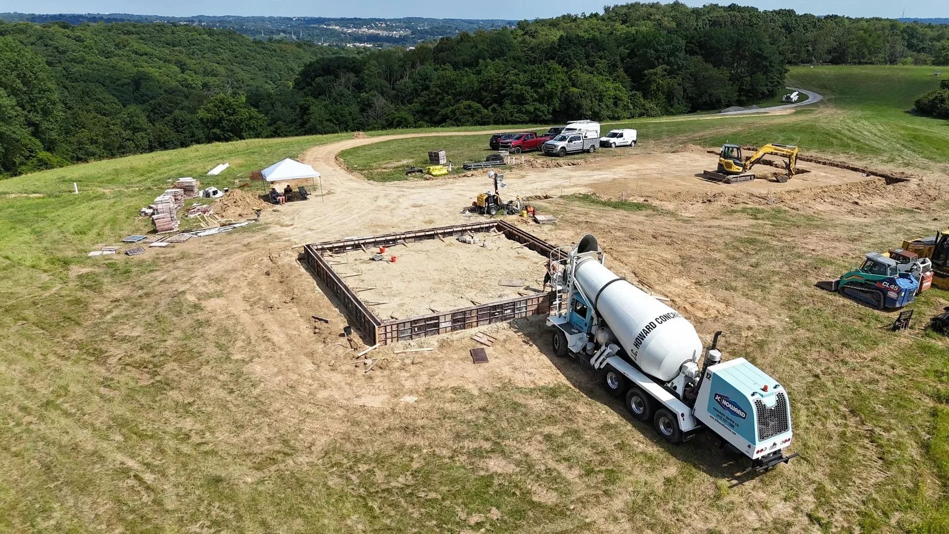Construction site: concrete truck pouring concrete into a building foundation on a grassy hilltop.