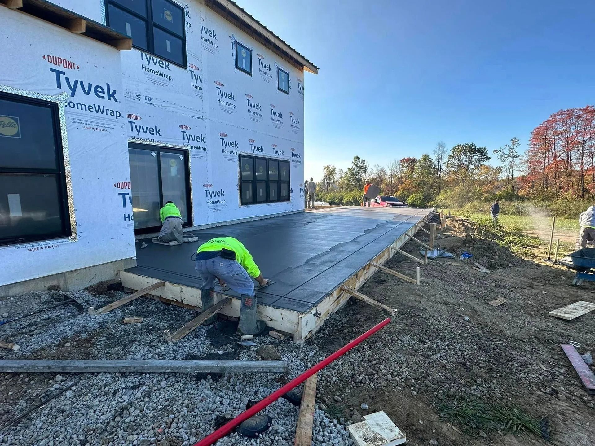 Construction workers pouring concrete for a patio outside a two-story house.